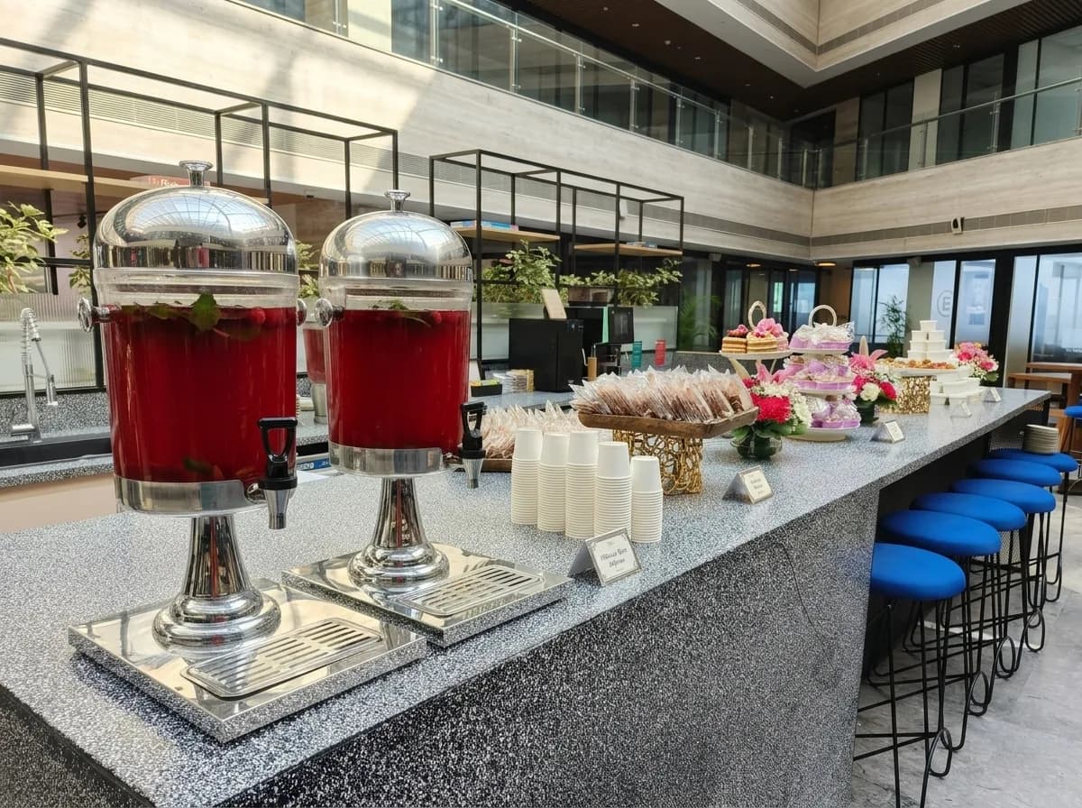 Glass beverage dispensers and dessert tiers on a stone counter in a corporate atrium