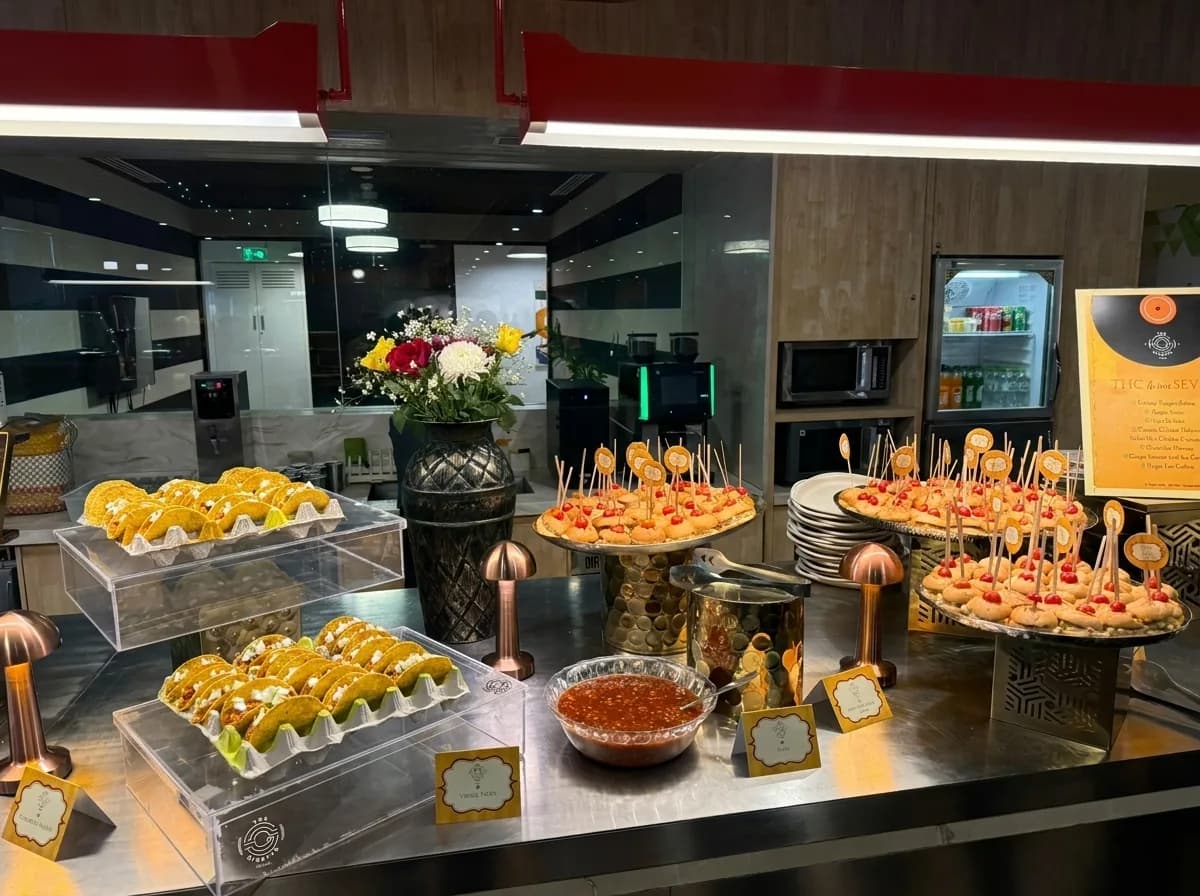 Glass cases of mithai and skewered canapés on an office service counter dressed with flowers