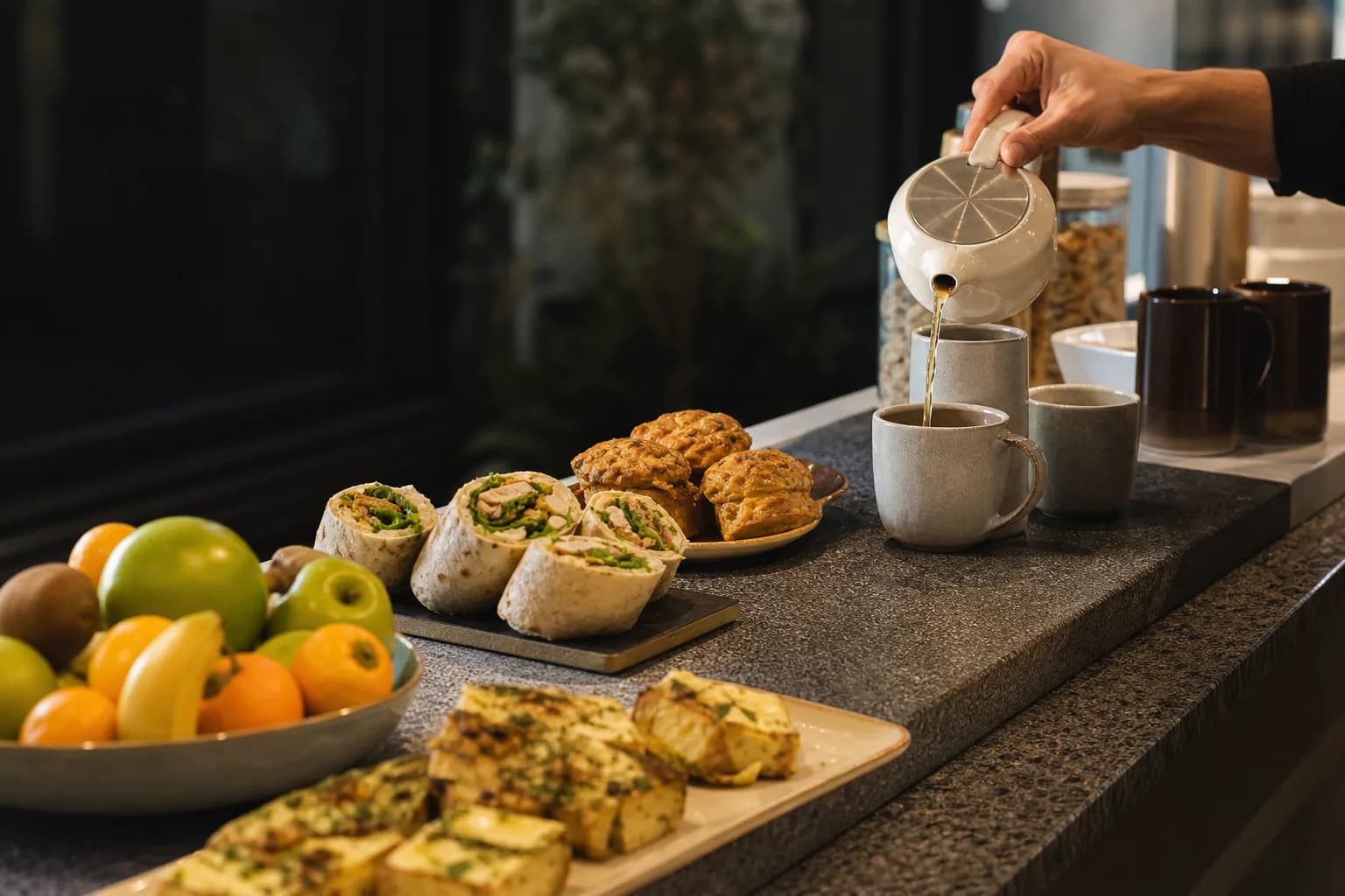 Afternoon tea being poured beside wraps, savoury bites and a bowl of fruit